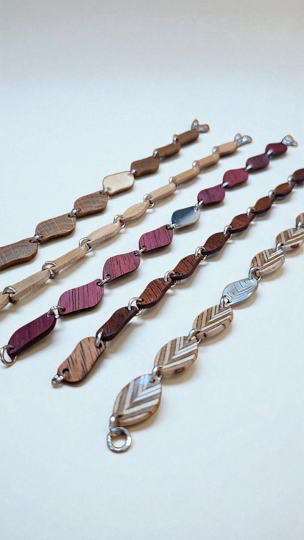 Handgemaakte houten armbanden van resthout en zilver uit het TimberRing atelier, naast elkaar gelegd. Elk schakeltje is uniek in houtsoort en tekening.